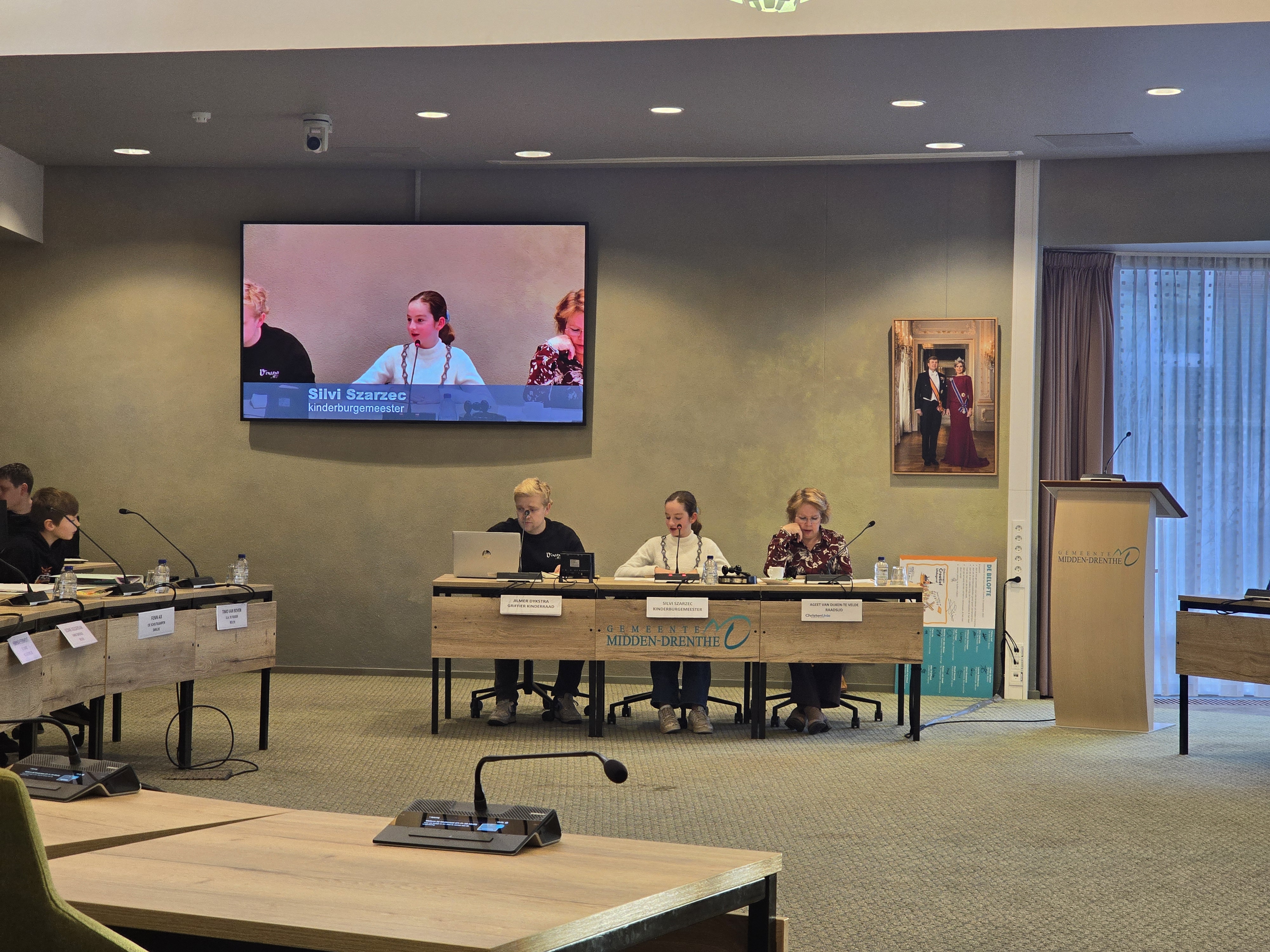 kinderburgemeester zit kinderraad voor, links van haar de griffier, rechts de voorzitter van de kinderraad