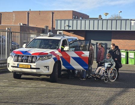 grote politieauto met open deur en daarnaast kinderen en een jongen in een rolstoel
