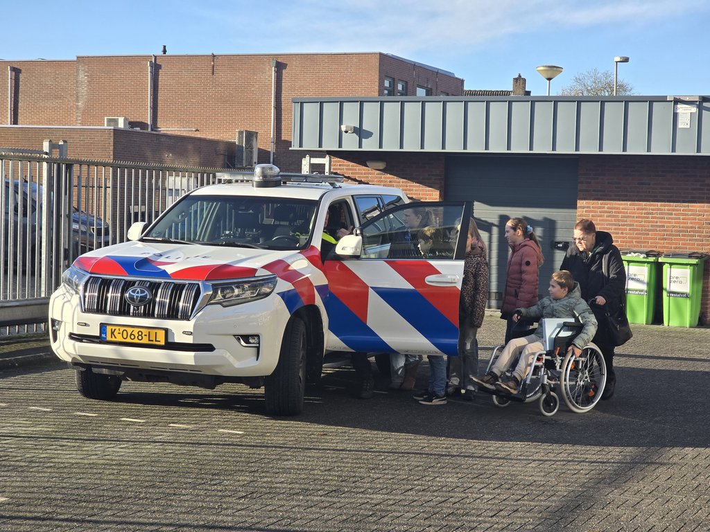 grote politieauto met open deur en daarnaast kinderen en een jongen in een rolstoel